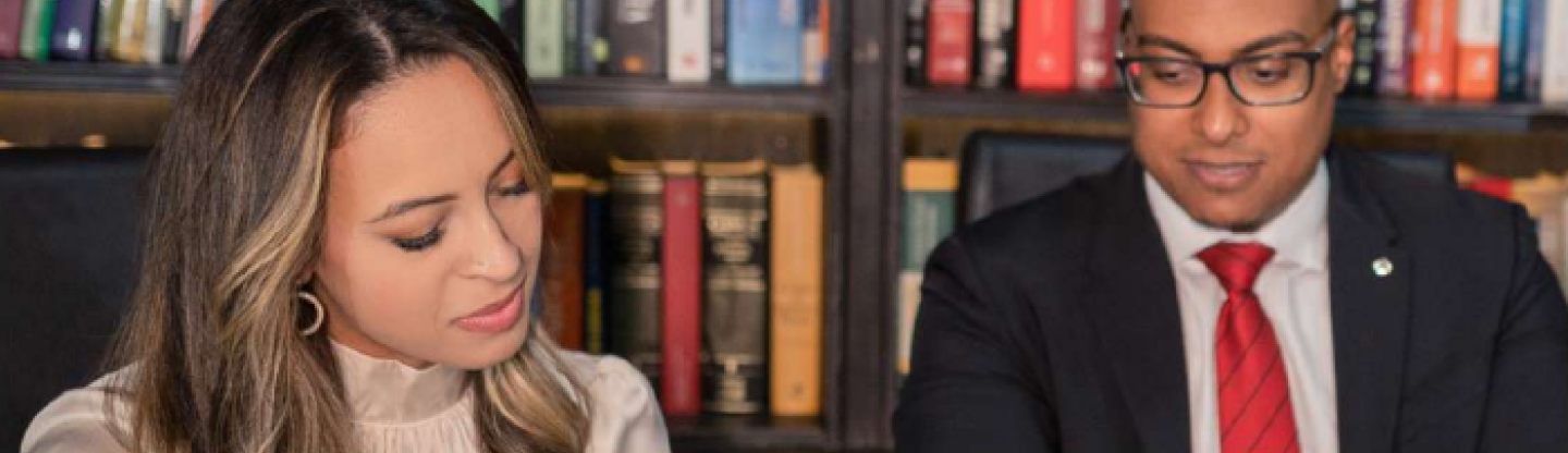 Dois advogados: um homem e uma mulher, olhando para algo em cima de uma mesa.